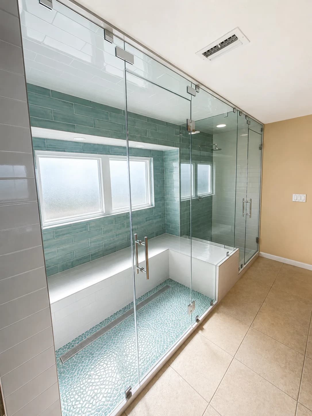 Frameless glass shower enclosure with teal subway tile, built-in bench and pebble mosaic floor in a Sarasota bathroom