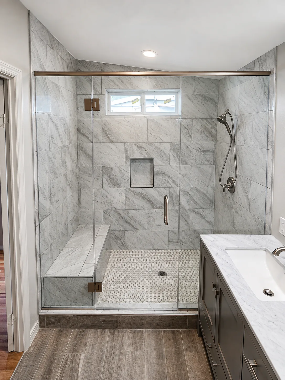 Custom frameless shower enclosure with wall-mounted hinges, tiled bench and hexagon mosaic floor in a Sarasota bathroom