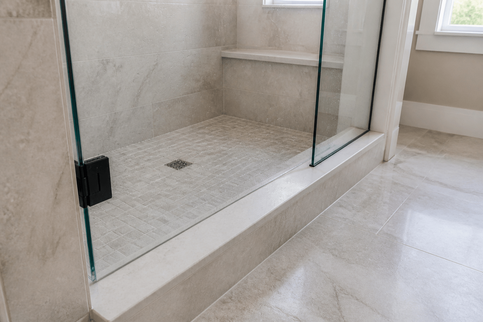 Frameless shower glass on a smooth one-piece stone sill pitched toward the tiled shower floor.