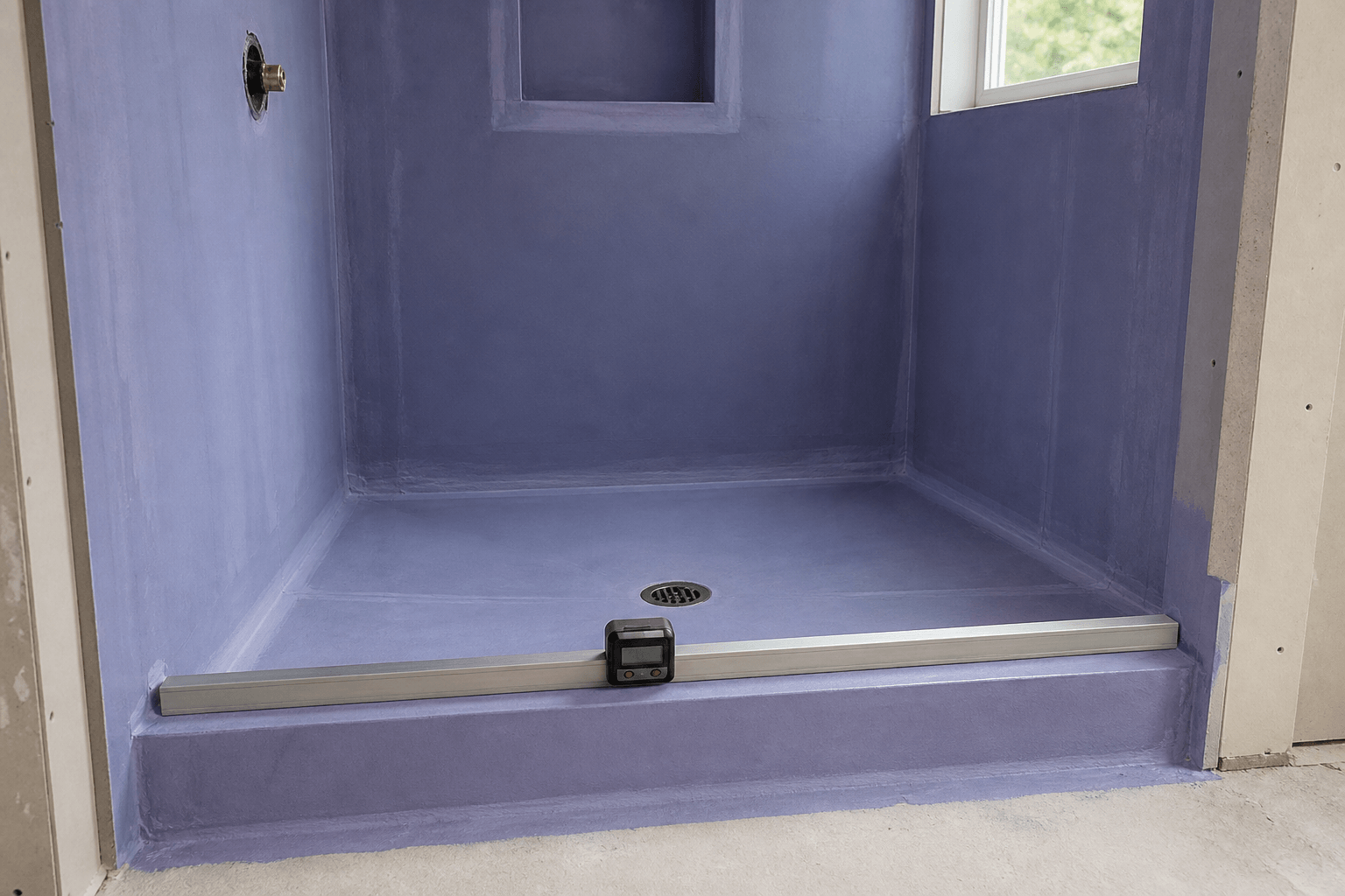 Digital level and straightedge checking an untiled shower curb's inward slope and alignment.